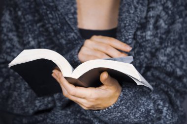 Gri örme kazak giyen genç bir kadın kitap okuyor.