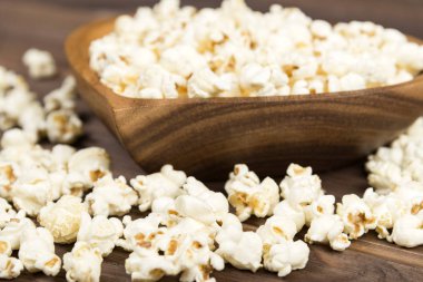 Tahta bir masa üzerinde kalp şeklinde kahverengi ahşap plaka patlamış mısır. Patlamış mısır masaya serilir.