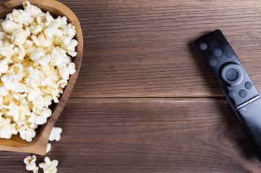 Ahşap bir kase ve ahşap bir masa üzerinde bir televizyon uzaktan kumanda kalp şeklinde patlamış mısır