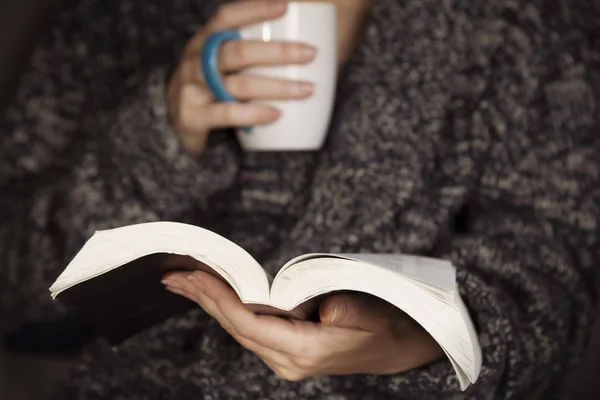 Gri örme kazak giyen genç bir kadın kitap okuyor.