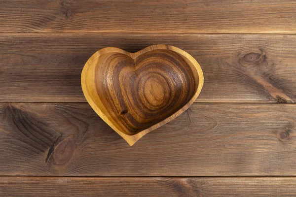 Wooden plate in the form of a heart on a wooden background, top view — Stock Photo, Image