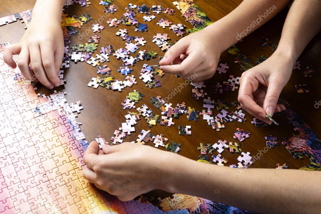 Minsk, Belarus, Aug. 11, 2019. Children and adult hands stack a color puzzle on a wooden table