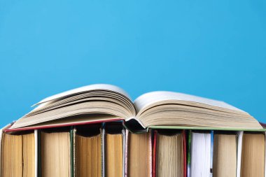 Hardback kitaplar, ahşap güverte masa ve mavi arka plan üzerinde ham kitaplar basit kompozisyon. Yazıtsız kitap istifleme, boş omurga. Okula geri dön. Açık kitap. Metin için yer