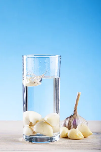 Mavi bir arka plan üzerinde bir bardak su sarımsak, sarımsak suyu, hastalık önleme. Baş sarımsak, sarımsak karanfil