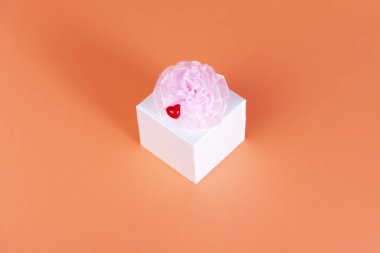 Turuncu arka planda beyaz kare kutu. Pembe bir fiyonk ve kırmızı küçük kalp.