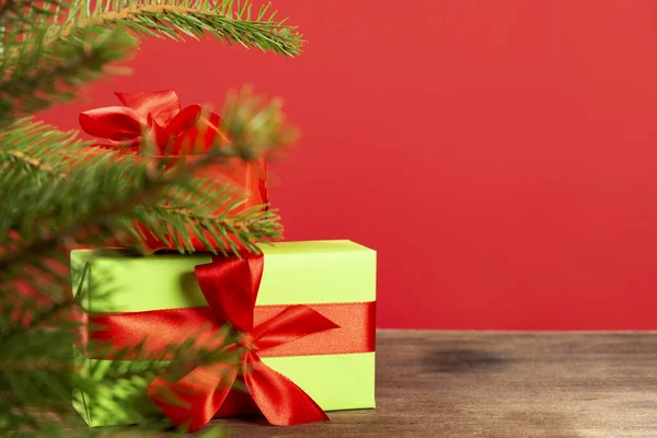Zapakowany zielony prezent z czerwoną wstążką leży pod choinką na drewnianej podłodze — Zdjęcie stockowe