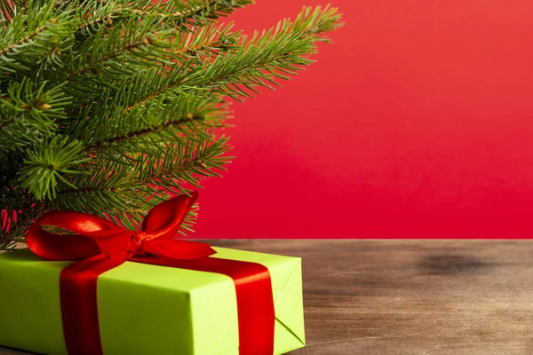 Świąteczna kompozycja. Zielone pudełko pod choinką na drewnianym stole w pobliżu czerwonego tła. prezent świąteczny — Zdjęcie stockowe