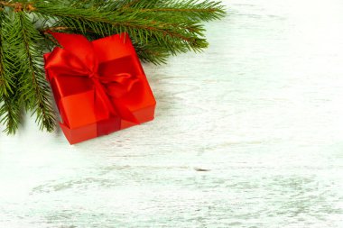 Köknar dallarının yanındaki ahşap zeminde kırmızı bir fiyonk olan kırmızı hediye kutusu. Yukarıdan bak. Noel kompozisyonu