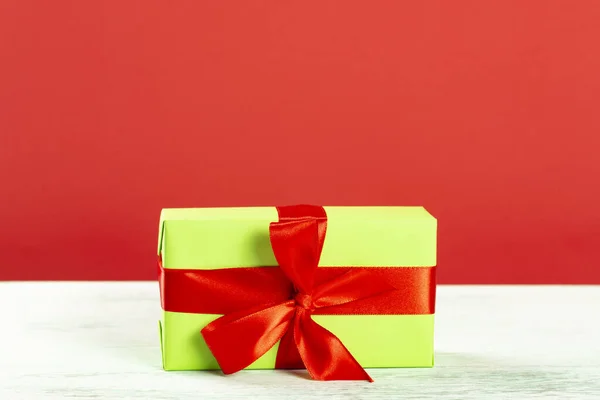 Świąteczna kompozycja. Zielone pudełko z czerwoną wstążką na czerwonym tle. Widok z boku. prezent świąteczny — Zdjęcie stockowe
