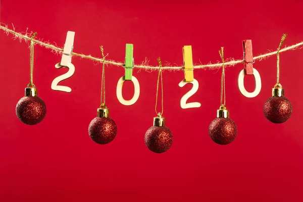 Christmas composition with wooden figures 2020. Figures hang on clothespins on a twine with red balls on a red background