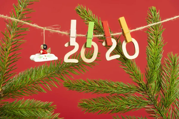 Christmas composition with wooden figures 2020. Figures hang on clothespins on a twine with a Christmas tree branch on a red background
