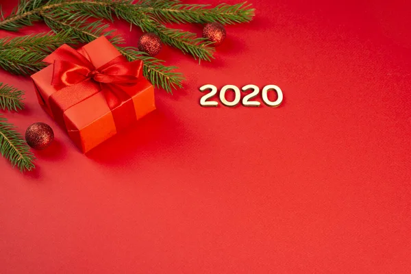 Composición navideña. Regalo rojo, ramas de abeto, adornos rojos sobre fondo rojo. Figuras de madera 2020 Navidad, invierno, concepto de año nuevo. Plano, vista superior, espacio para copiar — Foto de Stock