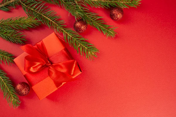 Vánoční kompozice. Červený dárek, smrkové větve, červené dekorace na červeném pozadí. Vánoce, zima, novoroční koncept. Byt ležel, horní pohled, kopírovací prostor — Stock fotografie