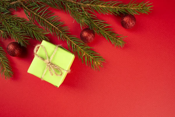 Vánoční kompozice. Zelený dárek, smrkové větve, červené ozdoby na červeném pozadí. Vánoce, zima, novoroční koncept. Byt ležel, horní pohled, kopírovací prostor — Stock fotografie