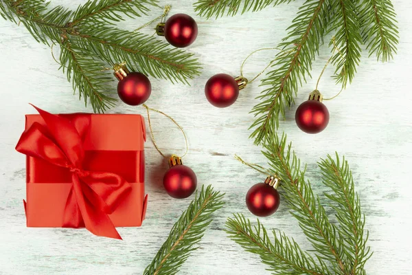 Vánoční kompozice. Červený dárek, smrkové větve, červené ozdoby na světlém dřevěném pozadí. Vánoce, zima, novoroční koncept. Byt ležel, horní pohled — Stock fotografie