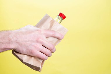 Sarı arka planda bir kese kağıdında alkol şişesi olan bir erkek. Kopyalama alanı ile görüntüyü kapat.