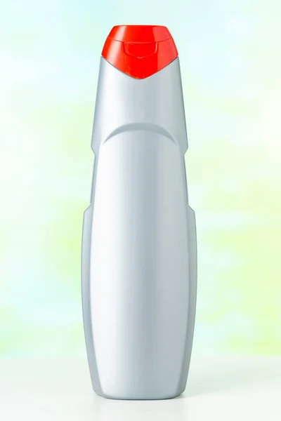 Безымянная серая пластиковая бутылка с красной крышкой моющего средства на цветном фоне — стоковое фото