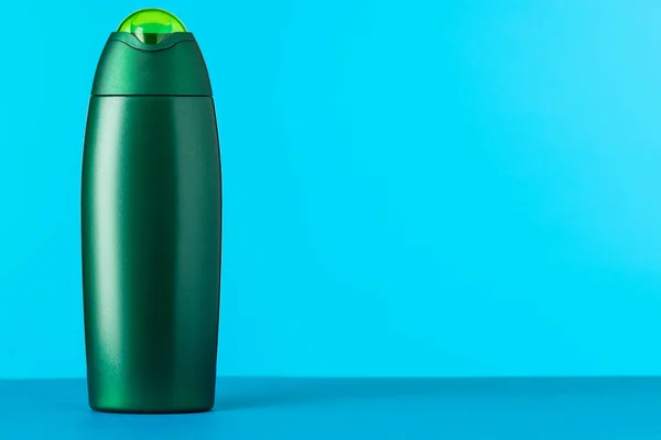 An unnamed green plastic bottle for a cosmetic product on a blue background with place for text