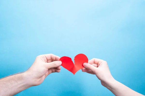Мужская и женская руки разбивают бумагу красным сердцем на синем фоне с местом для текста. Проблемы отношений — стоковое фото