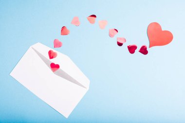 Açık mavi arka planda beyaz bir zarftan kırmızı konfeti kalpler uçar. Sevgililer Günü. Aşk konsepti Hediye, sevgiliye mesaj