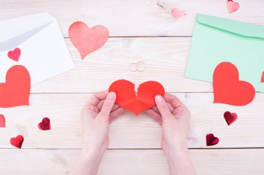 Kadın elleri kırık bir kalbi tahta bir masada alyansla tutar. Evlilik sorunları, boşanma.