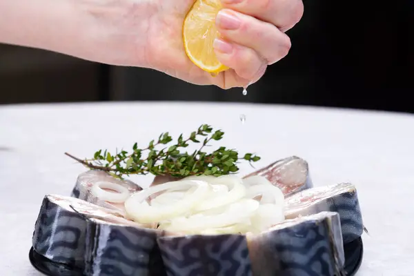 Ruka šéfkuchaře vymačká citrón na makrelu s cibulí — Stock fotografie
