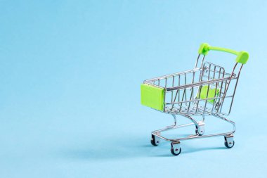 Mavi arka planda boş bir alışveriş arabası, metin için yeri olan renkli arkaplanda izole edilmiş mini metal tramvay.