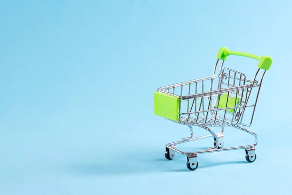 Prázdný nákupní vozík na modrém pozadí, mini kovový vozík izolovaný na barevném pozadí s místem pro text — Stock fotografie