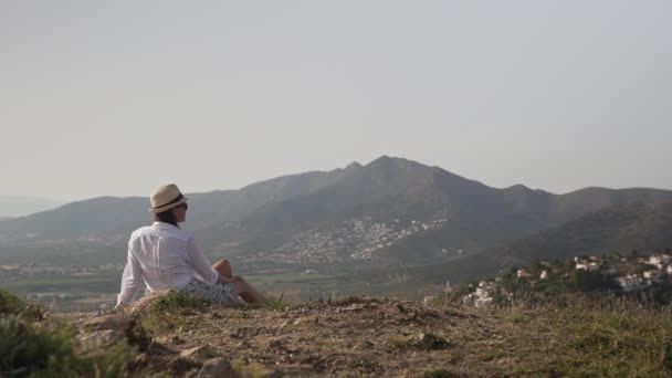 山の上に座っている女の子は 彼女の帽子をまっすぐに風景を賞賛 — ストック動画