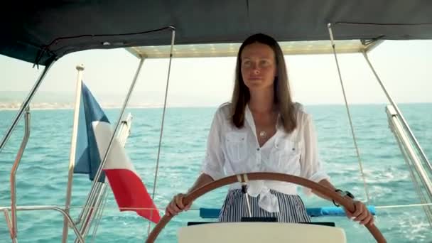 美丽的女孩控制一个游艇站在掌舵 从后海 法国国旗 — 图库视频影像