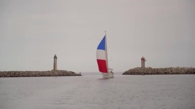Fransa bayraklı yelkenli yat iki deniz fenerleri arasında bir limanda yelken