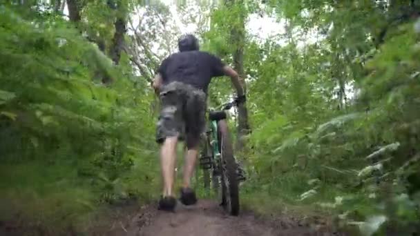 Ein Radfahrer trägt ein Fahrrad neben sich bergauf im Wald — Stockvideo