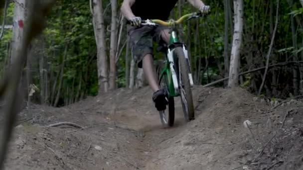 Cyclist on a green bike descends along an dirt road down, surrounded by trees — Stock Video