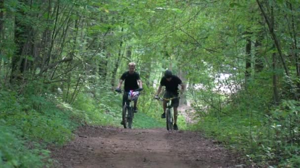 2人のサイクリストが森林道路に沿って走る — ストック動画
