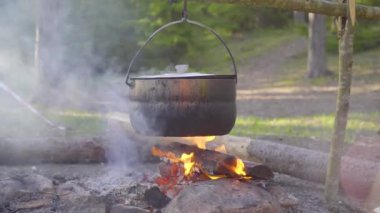Ateşin üzerinde bir kazan asılı, ateş etrafına sarılmış.