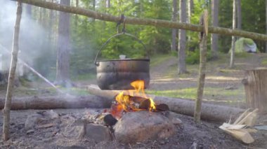 Ateşin üzerinde bir kazan asılı, ateş etrafına sarılmış.