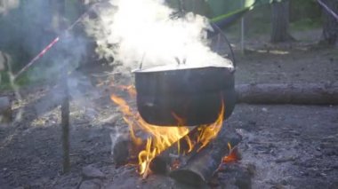 Ateşin üzerinde bir kazan asılı, ateş etrafına sarılmış.