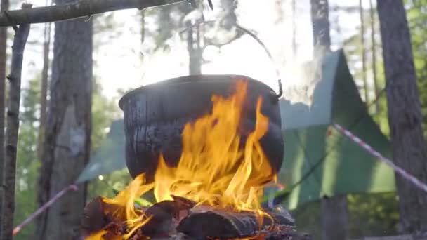 Uma panela pendurada em um pau sobre o fogo, o fogo envolto em torno dele — Vídeo de Stock