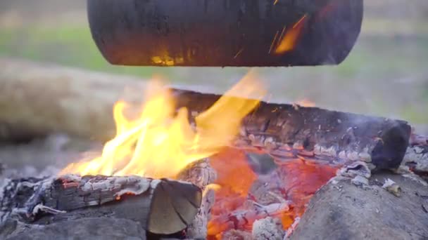 Una olla colgando de un palo sobre el fuego, el fuego envuelto alrededor de ella — Vídeos de Stock