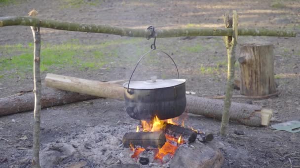 Pot tergantung pada tongkat di atas api, api membungkus sekelilingnya — Stok Video