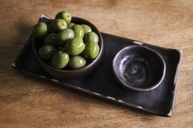 Yeşil Zeytin ahşap arka plan üzerinde siyah bir seramik kase. Zeytin bir restoranda servis