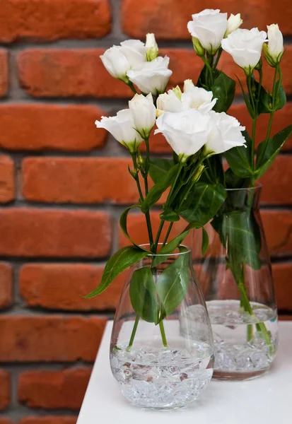 Білі квіти еустоми в склі на фоні червоної цегляної стіни — стокове фото