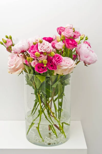 Bouquet of pink roses, peony flowers in glass vase on a shelf ag
