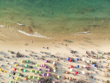 Kum üzerinde kalabalık bir plaj, şemsiye ve insanlar havadan görünümü