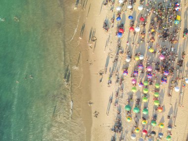 Kum üzerinde kalabalık bir plaj, şemsiye ve insanlar havadan görünümü