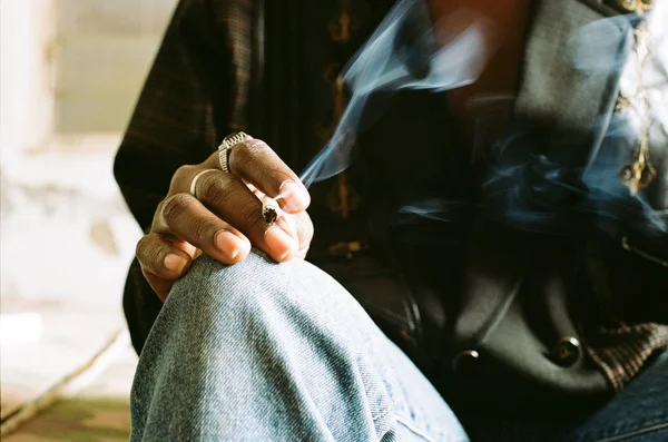 戒指覆盖的手指休息在褪色的蓝色牛仔裤 包裹在点燃的香烟 — 图库照片