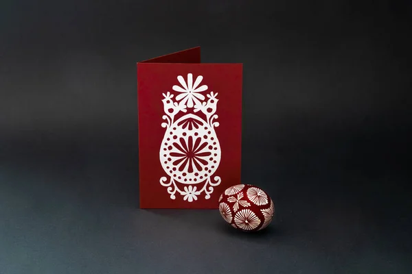 Traditional lithuanian Easter egg natural  painted with beeswax white and braun in pattern and red postcard with white paper cut, where are representing  egg, sun, birds and flowers -symbols of spring