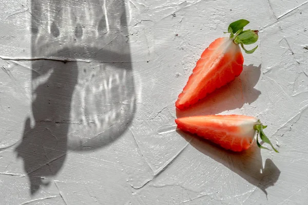 Arrangement with strawberry pieces and a glass shadow on a white table