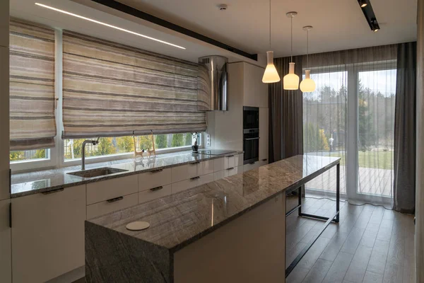 Modern beautiful kitchen with home furnishings in luxury home. Desk for food preparation, sink, cooker, fridge, cabinets with drawers,  pendant lights and hood in a spacious bright room.