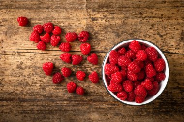 Kırsal ve ahşap arka planda bir kasede bir sürü ahududu var. Böğürtlenler kabın dışına yerleştirilir. Görüntü yukarıdan geliyor..